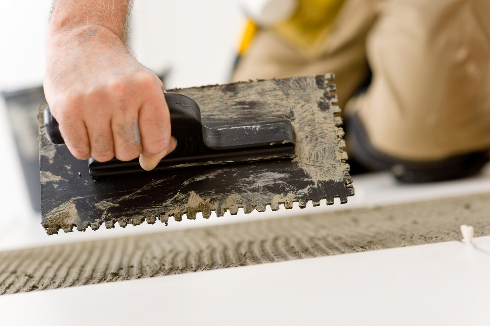 Home improvement, renovation - handyman laying tile, trowel with mortar